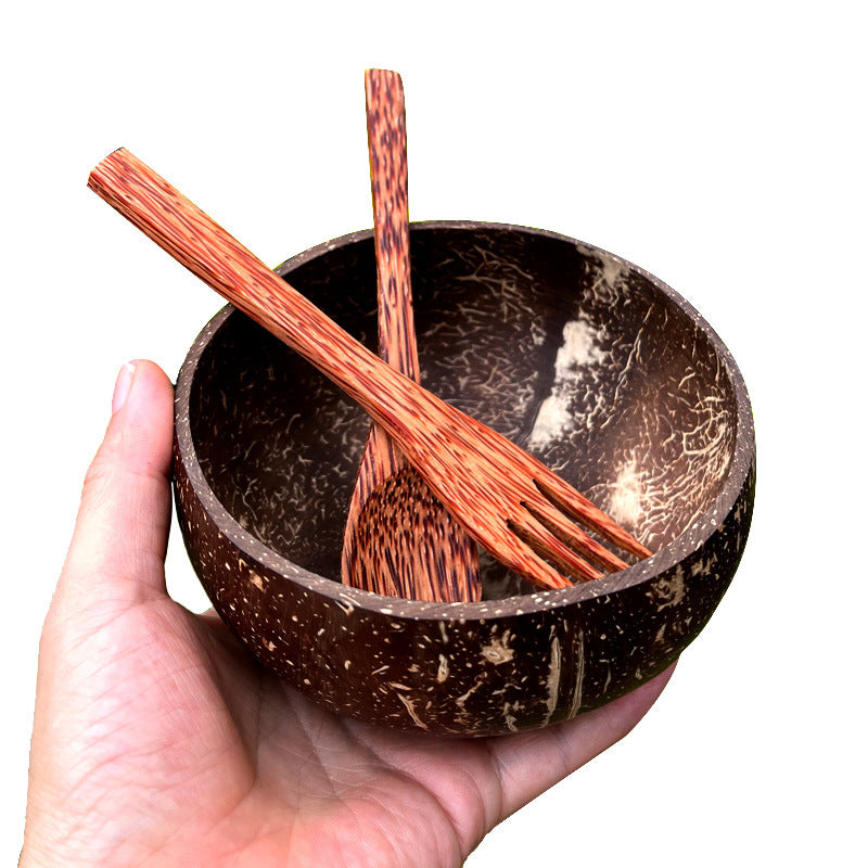 Hand holding natural coconut shell bowl with wooden spoon and fork