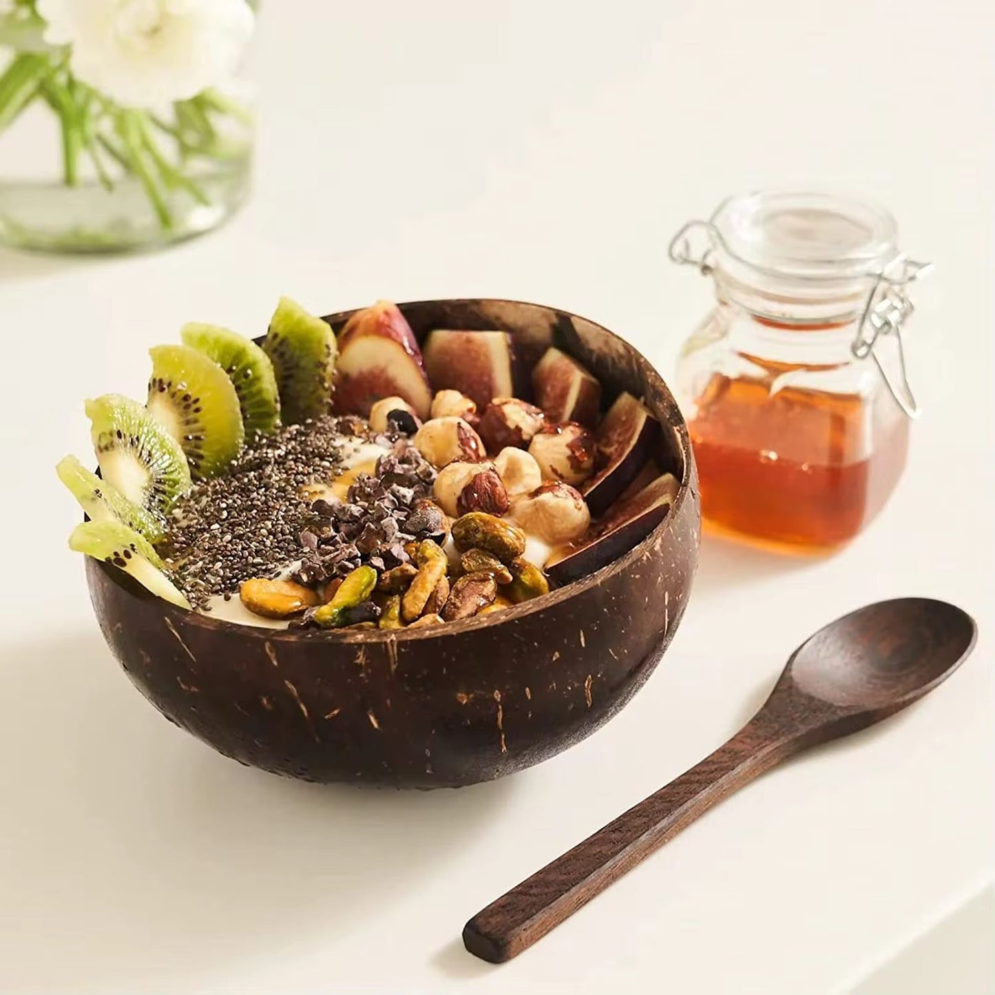 Handmade natural coconut bowl set with wooden spoon filled with smoothie, fresh fruits, nuts and seeds